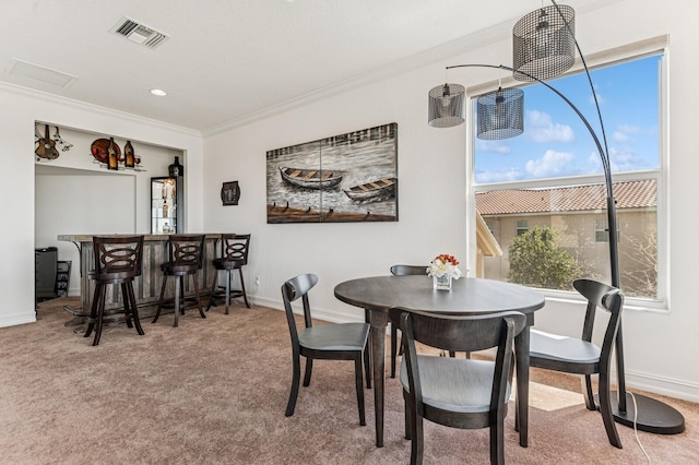 dining space featuring a dry bar, baseboards, visible vents, crown molding, and carpet floors