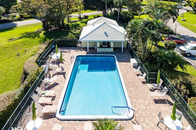 community pool with a patio, a lawn, and fence