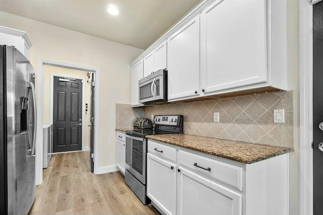 kitchen featuring light wood finished floors, dark stone counters, stainless steel appliances, white cabinets, and tasteful backsplash