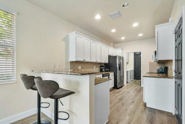 kitchen with visible vents, dark stone countertops, light wood-style floors, a peninsula, and white cabinets