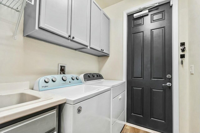 clothes washing area featuring a sink, wood finished floors, cabinet space, and washing machine and clothes dryer