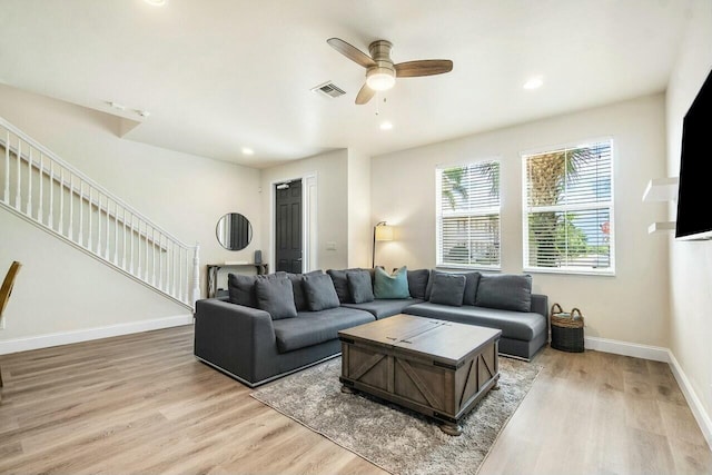 living room featuring visible vents, baseboards, stairway, light wood-style flooring, and a ceiling fan