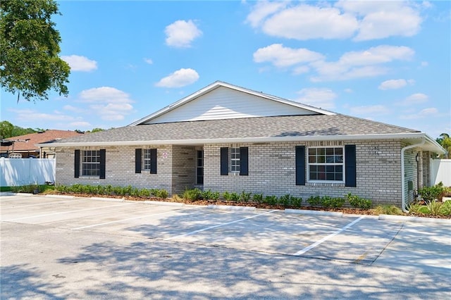 single story home with brick siding, fence, roof with shingles, and uncovered parking