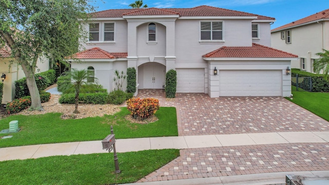 mediterranean / spanish home featuring decorative driveway, a tile roof, a front lawn, and stucco siding