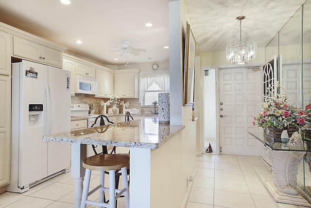 kitchen featuring white appliances, tasteful backsplash, a breakfast bar, light tile patterned flooring, and ceiling fan with notable chandelier