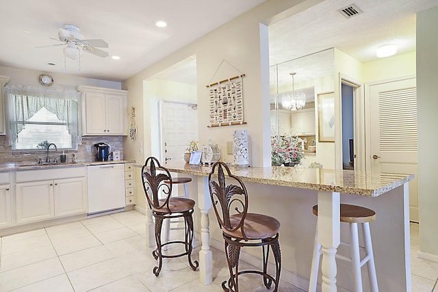 kitchen with light stone counters, white dishwasher, a breakfast bar, a sink, and visible vents