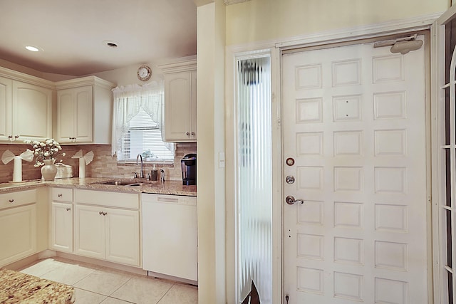 kitchen with light tile patterned floors, decorative backsplash, white dishwasher, a sink, and light stone countertops