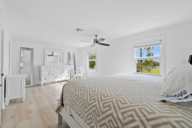 bedroom with crown molding, visible vents, a ceiling fan, a textured ceiling, and light wood-type flooring