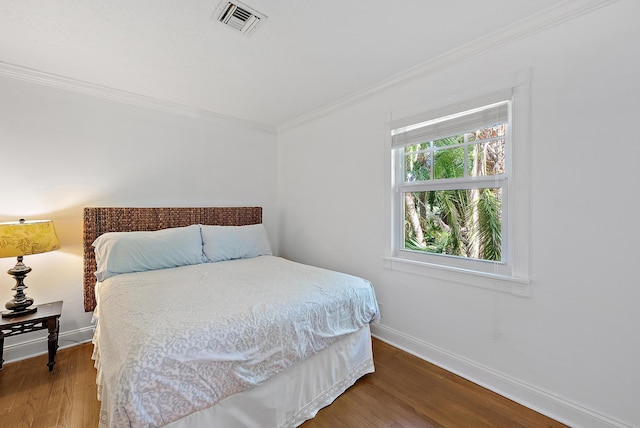 bedroom with baseboards, visible vents, wood finished floors, and ornamental molding