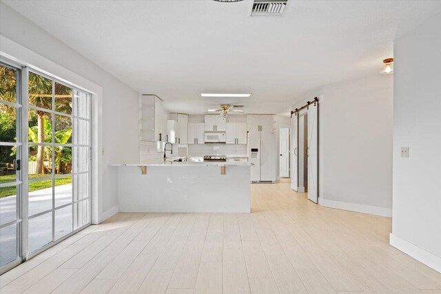 unfurnished living room featuring visible vents, a barn door, a ceiling fan, a sink, and baseboards