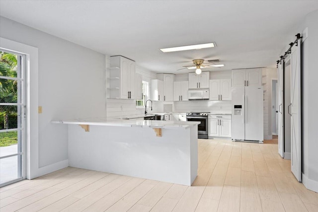 kitchen featuring white appliances, a peninsula, decorative backsplash, and a barn door