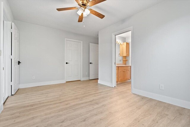 unfurnished bedroom with light wood finished floors, ensuite bath, baseboards, and a ceiling fan