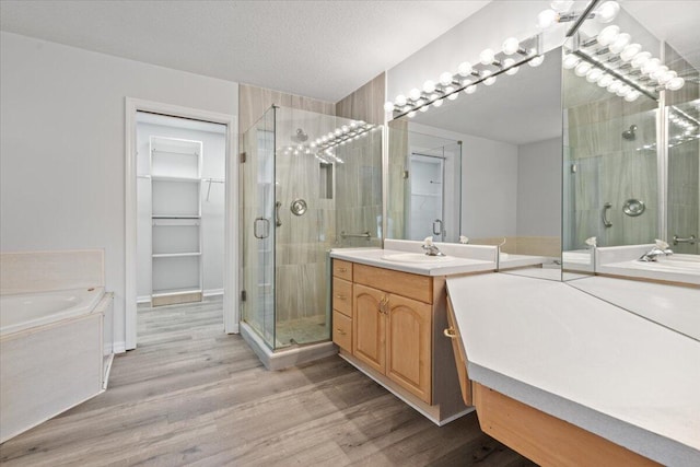 full bathroom featuring two vanities, a sink, a shower stall, a textured ceiling, and wood finished floors