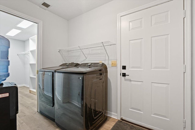 washroom featuring washing machine and dryer, laundry area, visible vents, baseboards, and light wood-style floors