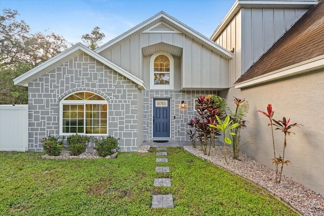 doorway to property with board and batten siding, a yard, and fence