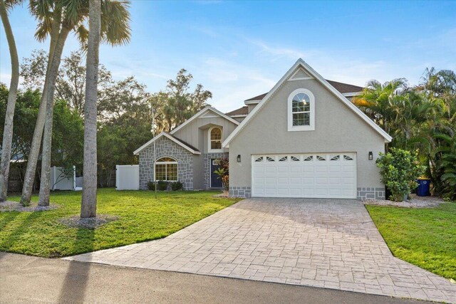 traditional-style house with decorative driveway, stucco siding, fence, a garage, and a front lawn