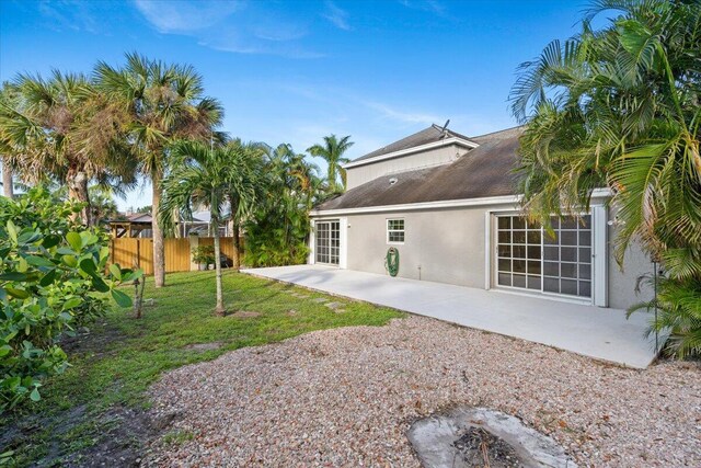 rear view of property with stucco siding, a patio, a lawn, and fence