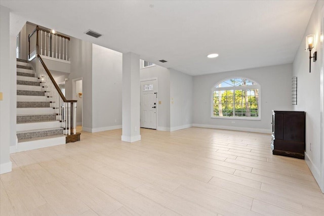 unfurnished living room featuring light wood-style floors, visible vents, stairs, and baseboards