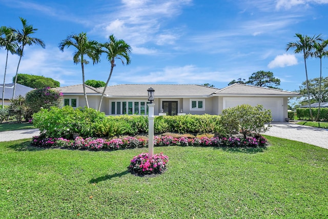 ranch-style home featuring a tile roof, stucco siding, a garage, driveway, and a front lawn