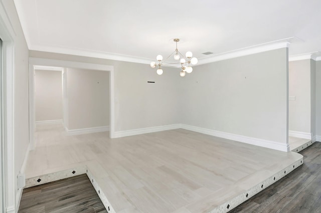 spare room with ornamental molding, a notable chandelier, baseboards, and wood finished floors