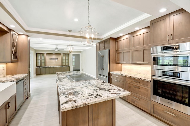 kitchen with appliances with stainless steel finishes, a raised ceiling, light stone countertops, and a center island