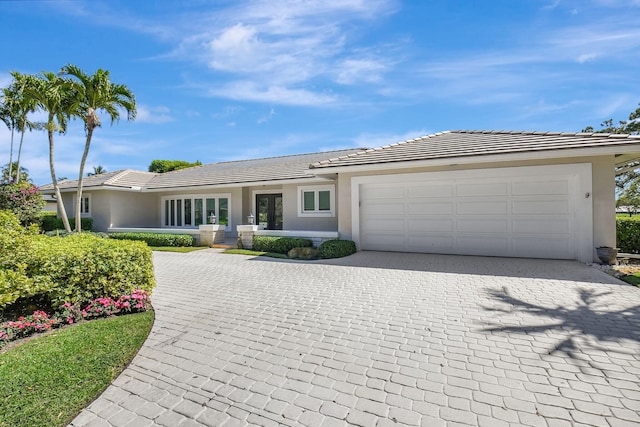 ranch-style home with a garage, decorative driveway, a tiled roof, and stucco siding