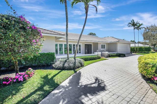 view of front facade with a garage, a tiled roof, decorative driveway, stucco siding, and a front yard