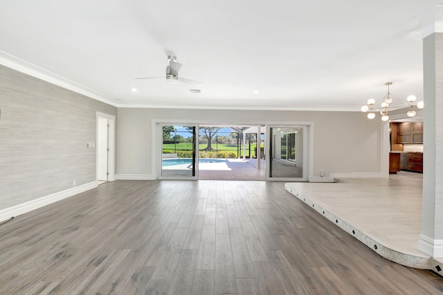 unfurnished living room featuring ceiling fan with notable chandelier, ornamental molding, wood finished floors, and baseboards