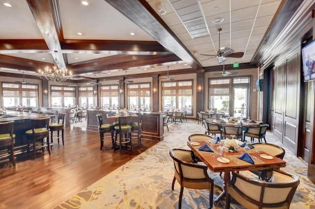 dining room with ceiling fan with notable chandelier, beamed ceiling, and wood finished floors