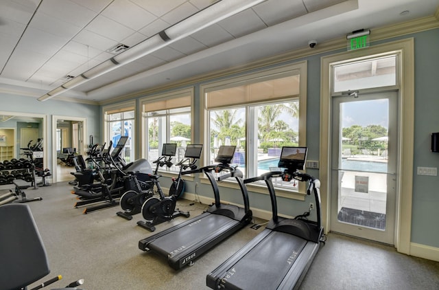 exercise room with a tray ceiling, ornamental molding, visible vents, and baseboards