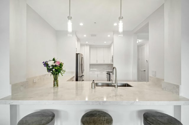 kitchen featuring freestanding refrigerator, a sink, a peninsula, and light stone countertops