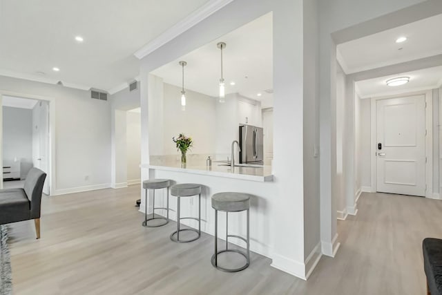 kitchen with a breakfast bar area, visible vents, ornamental molding, freestanding refrigerator, and white cabinets