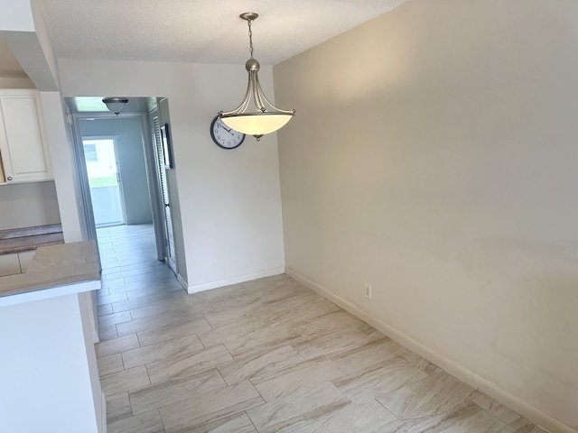 unfurnished dining area featuring a textured ceiling and baseboards