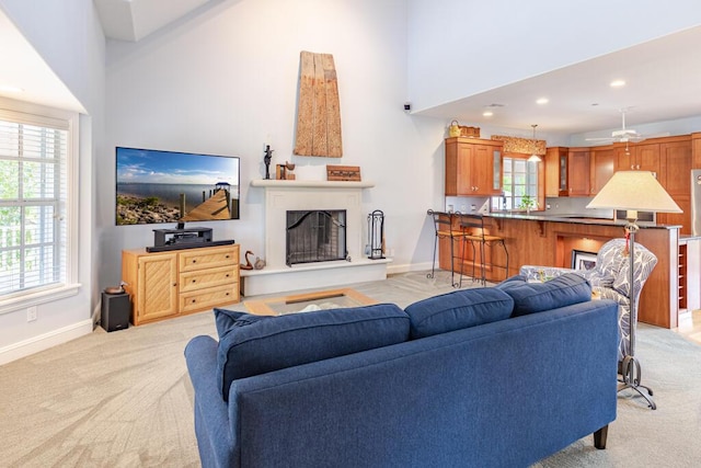 living room featuring light carpet, a towering ceiling, baseboards, and a fireplace with raised hearth