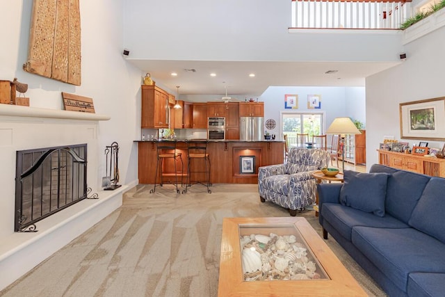 living room with a fireplace with raised hearth, a high ceiling, recessed lighting, and light colored carpet