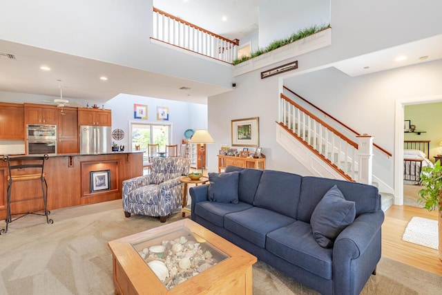 living room with light wood finished floors, visible vents, a towering ceiling, stairs, and recessed lighting