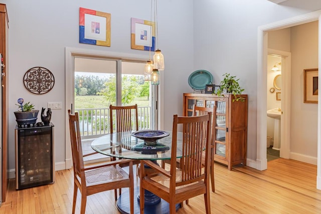 dining area featuring light wood-style floors, wine cooler, a towering ceiling, and baseboards