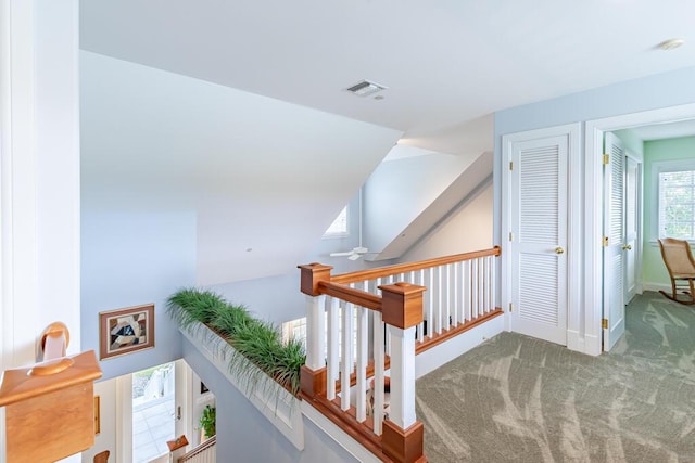 hall featuring an upstairs landing, carpet flooring, visible vents, and baseboards