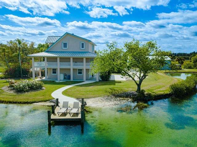 back of house featuring a lawn, metal roof, a water view, a standing seam roof, and stucco siding