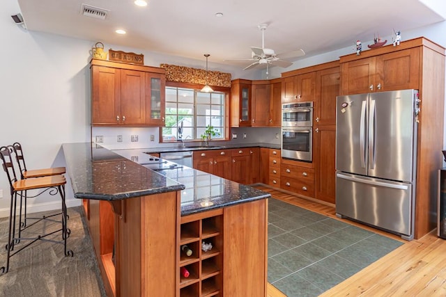 kitchen featuring stainless steel appliances, a peninsula, glass insert cabinets, and brown cabinets