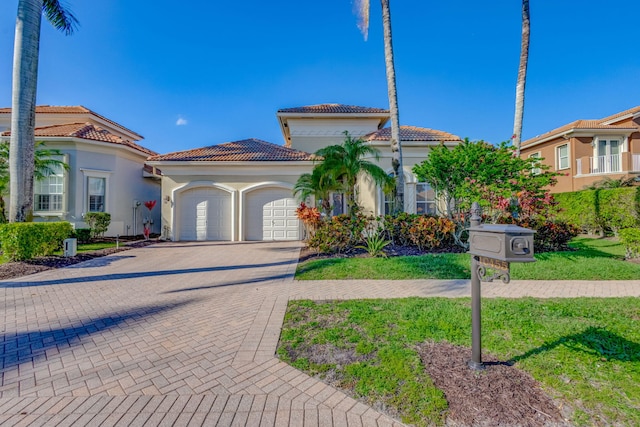 mediterranean / spanish-style home featuring a garage, stucco siding, a tile roof, decorative driveway, and a front yard