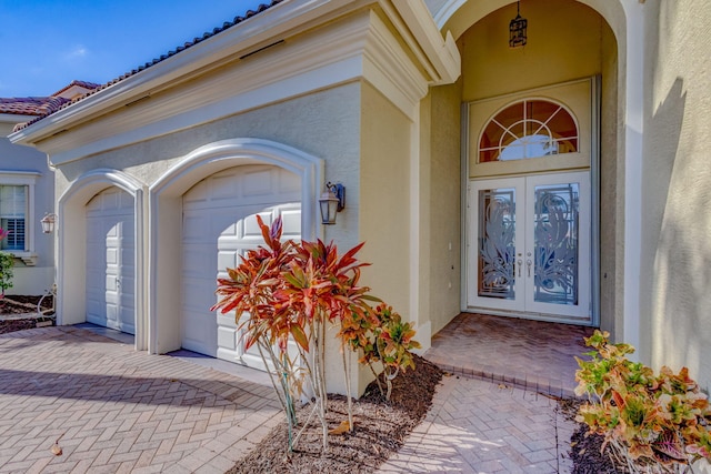 property entrance with decorative driveway, french doors, an attached garage, and stucco siding