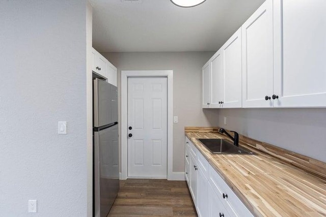 kitchen with dark wood-type flooring, a sink, freestanding refrigerator, and white cabinets