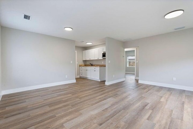 unfurnished living room featuring light wood-style flooring, visible vents, and baseboards