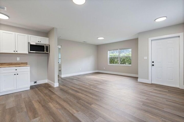 kitchen with stainless steel microwave, wood finished floors, white cabinetry, and baseboards