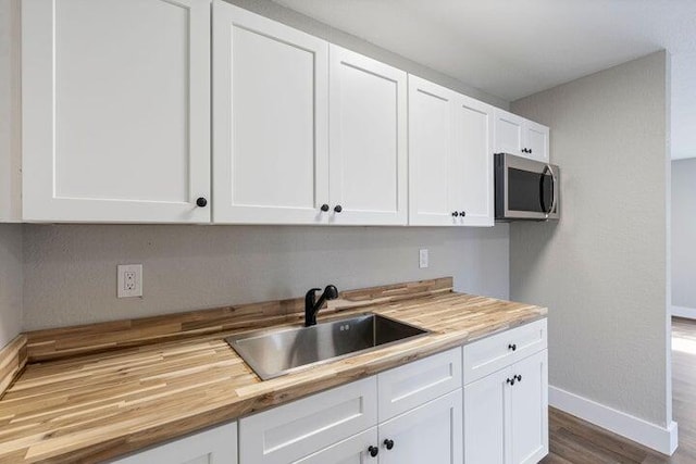 kitchen with stainless steel microwave, white cabinetry, a sink, butcher block countertops, and baseboards