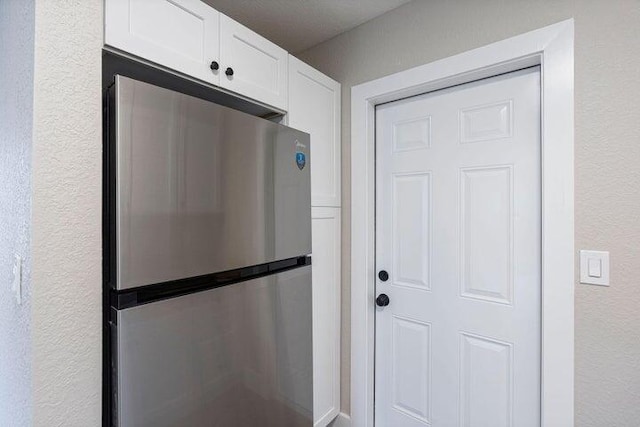 kitchen featuring a textured wall, white cabinetry, and freestanding refrigerator