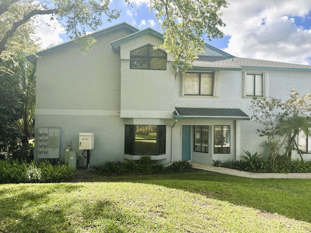 view of front of home with stucco siding, a shingled roof, and a front yard