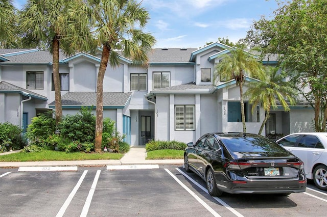 view of front of property featuring uncovered parking, roof with shingles, and stucco siding