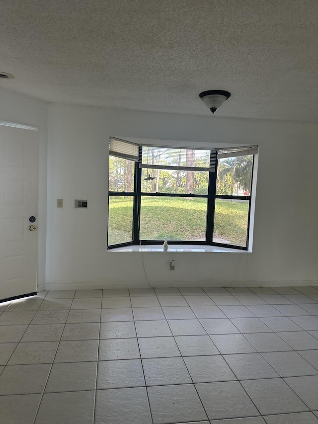 spare room with a textured ceiling, baseboards, and light tile patterned floors